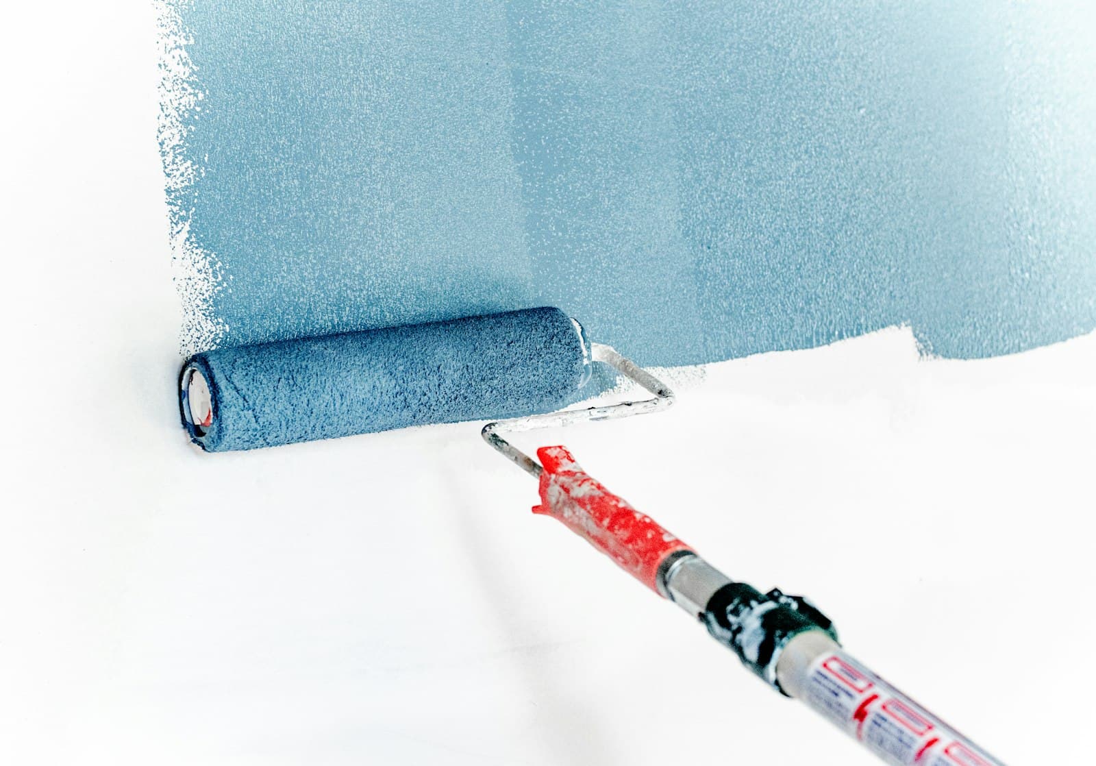 A roller applying fresh blue paint to a wall